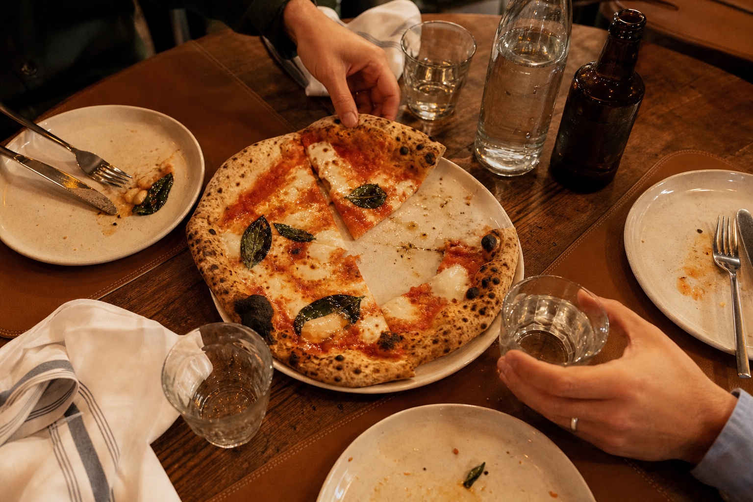 Una pizza condivisa su una tavola vissuta, tra bicchieri, posate e tovaglioli